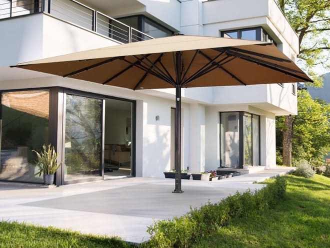 Beiger Sonnenschirm auf einer Terrasse vor einem Haus mit Garten